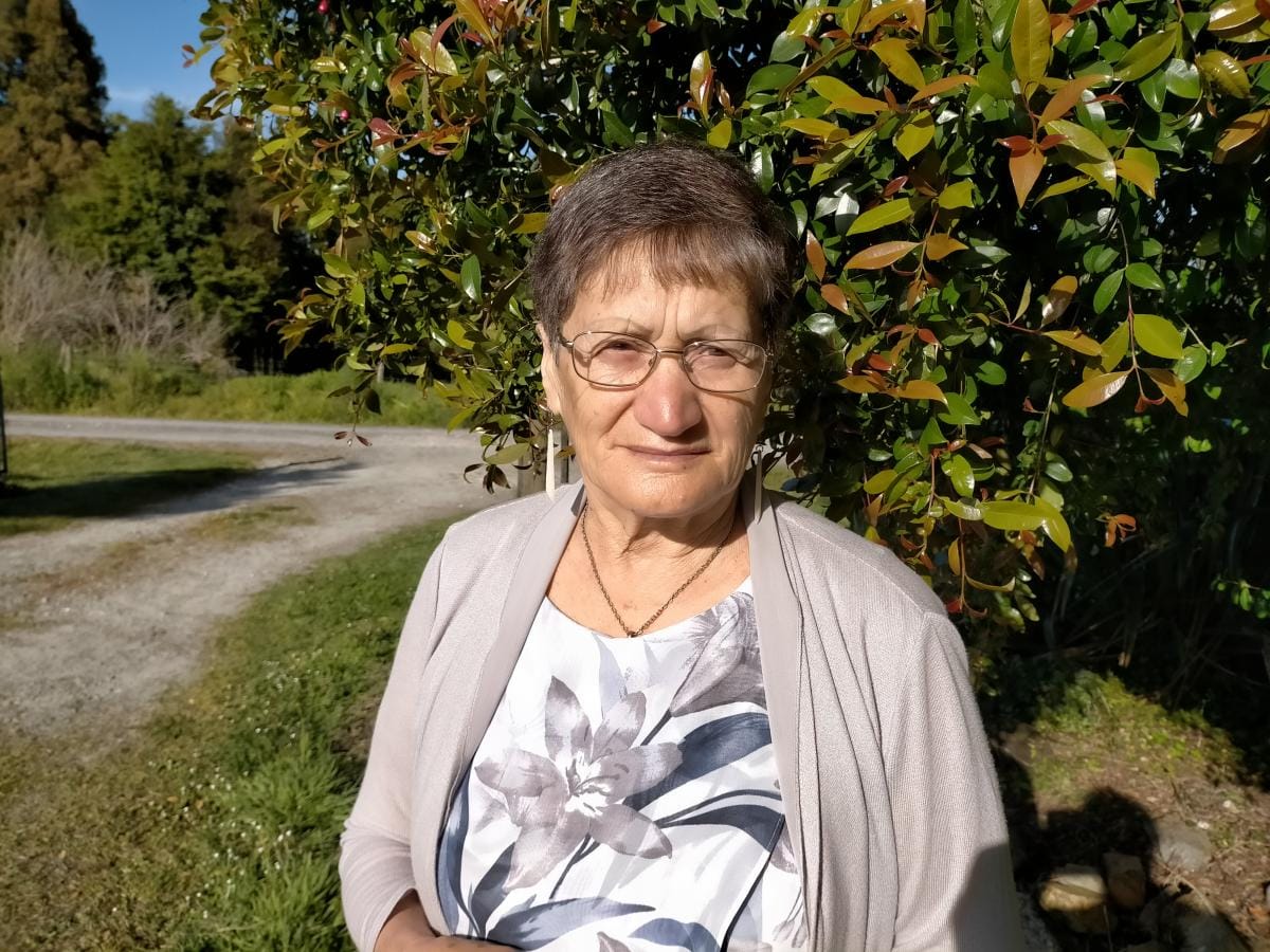 Rangi Davis in a floral white shirt and grey shrug standing in a grassy lawn.