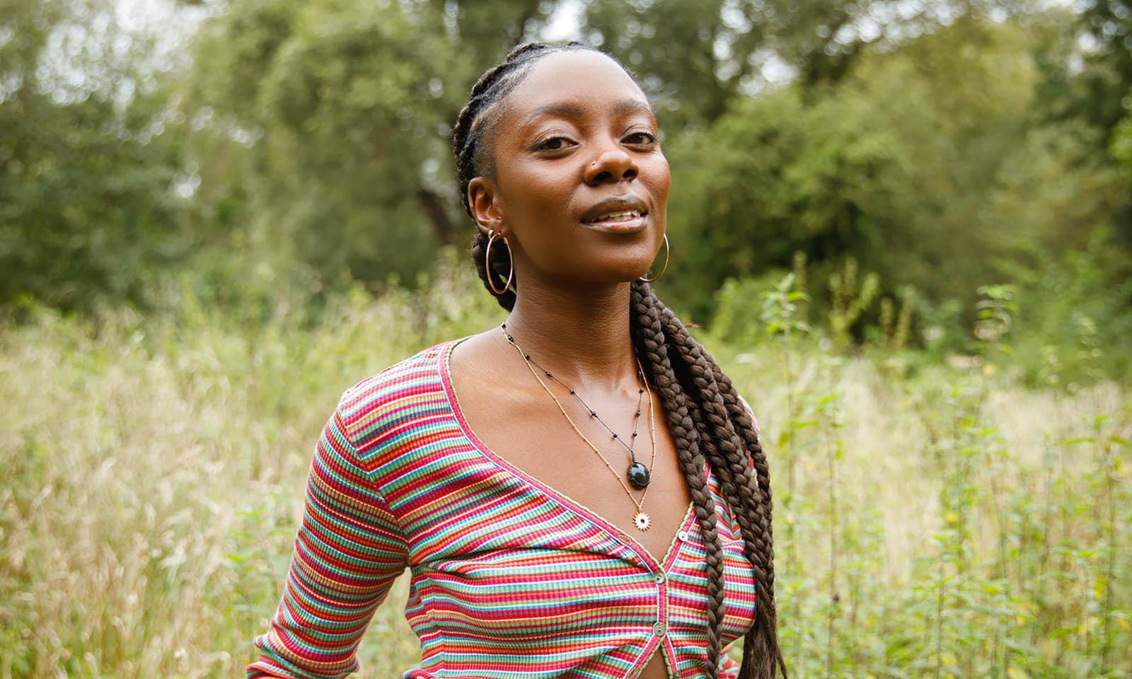 A photo of Joycelyn Longdon standing in a field filled with long grasses, posing for the camera.